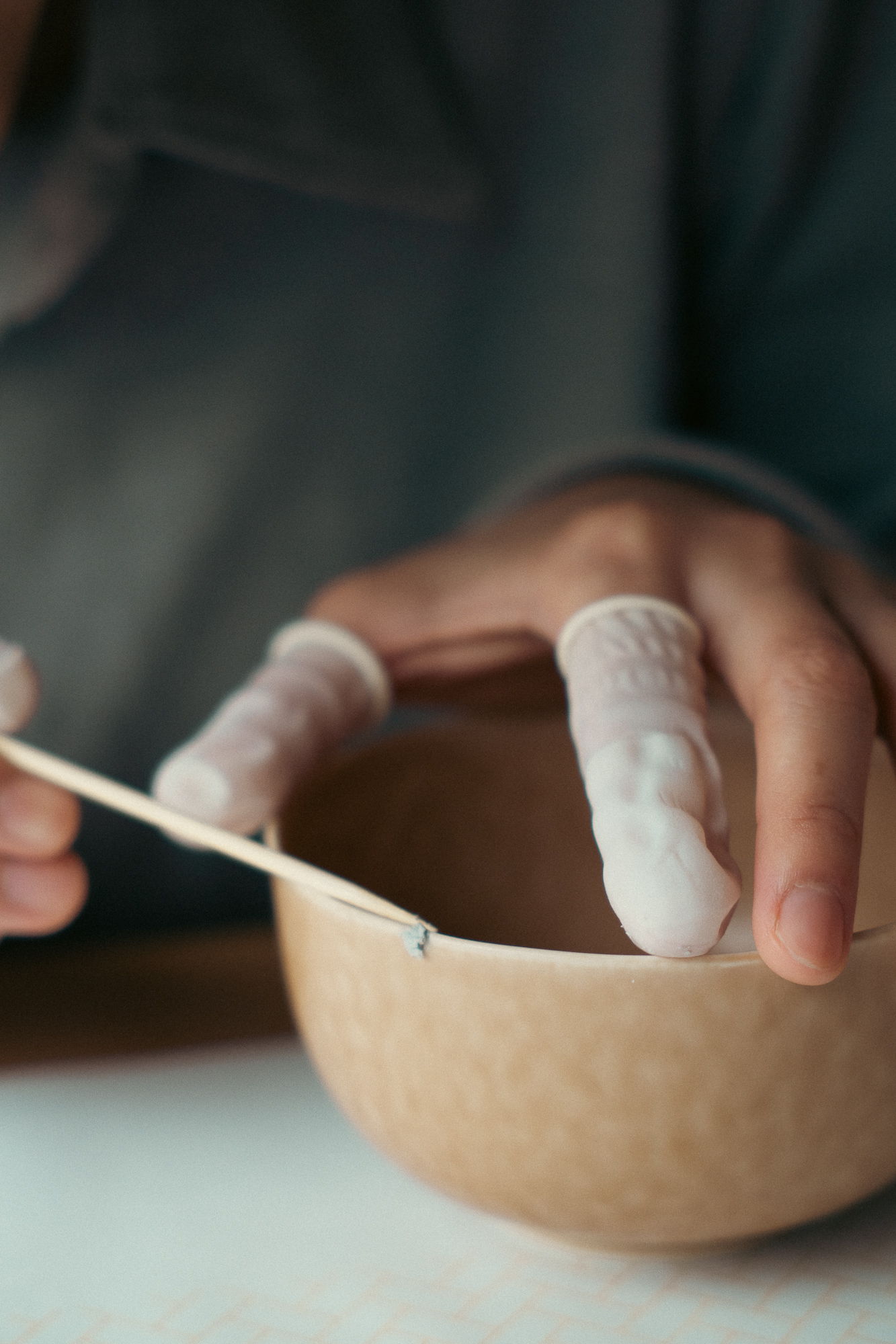 Person using a tool on a ceramic bowl with finger protectors.