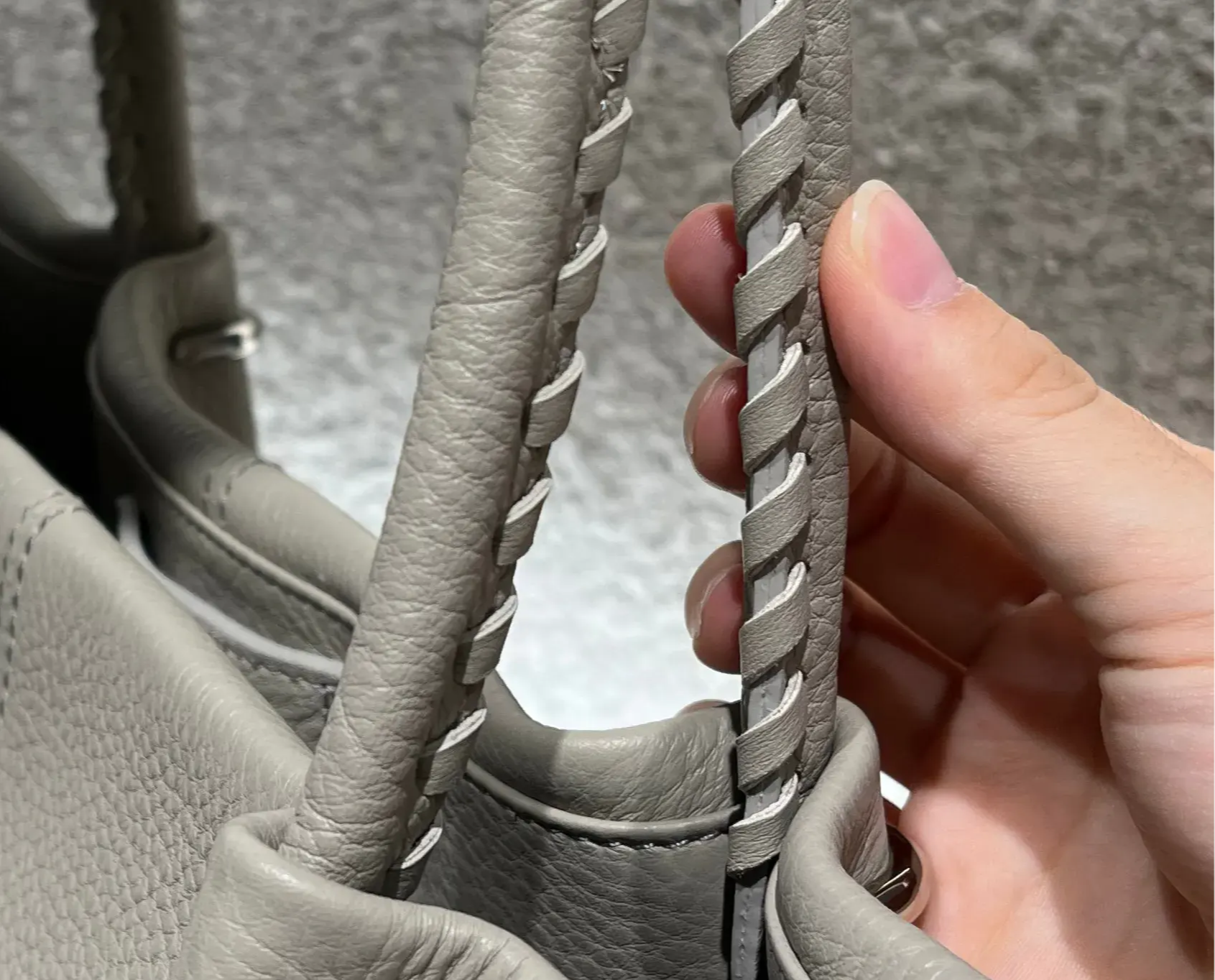 A hand holding a beige handbag with braided straps.