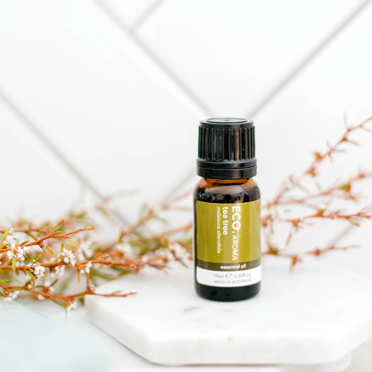 Image of tea tree essential oil bottle surrounded by flowers