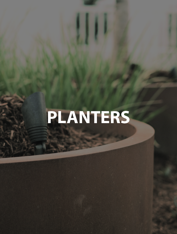 Planter with soil and a black gardening tool among green grass.