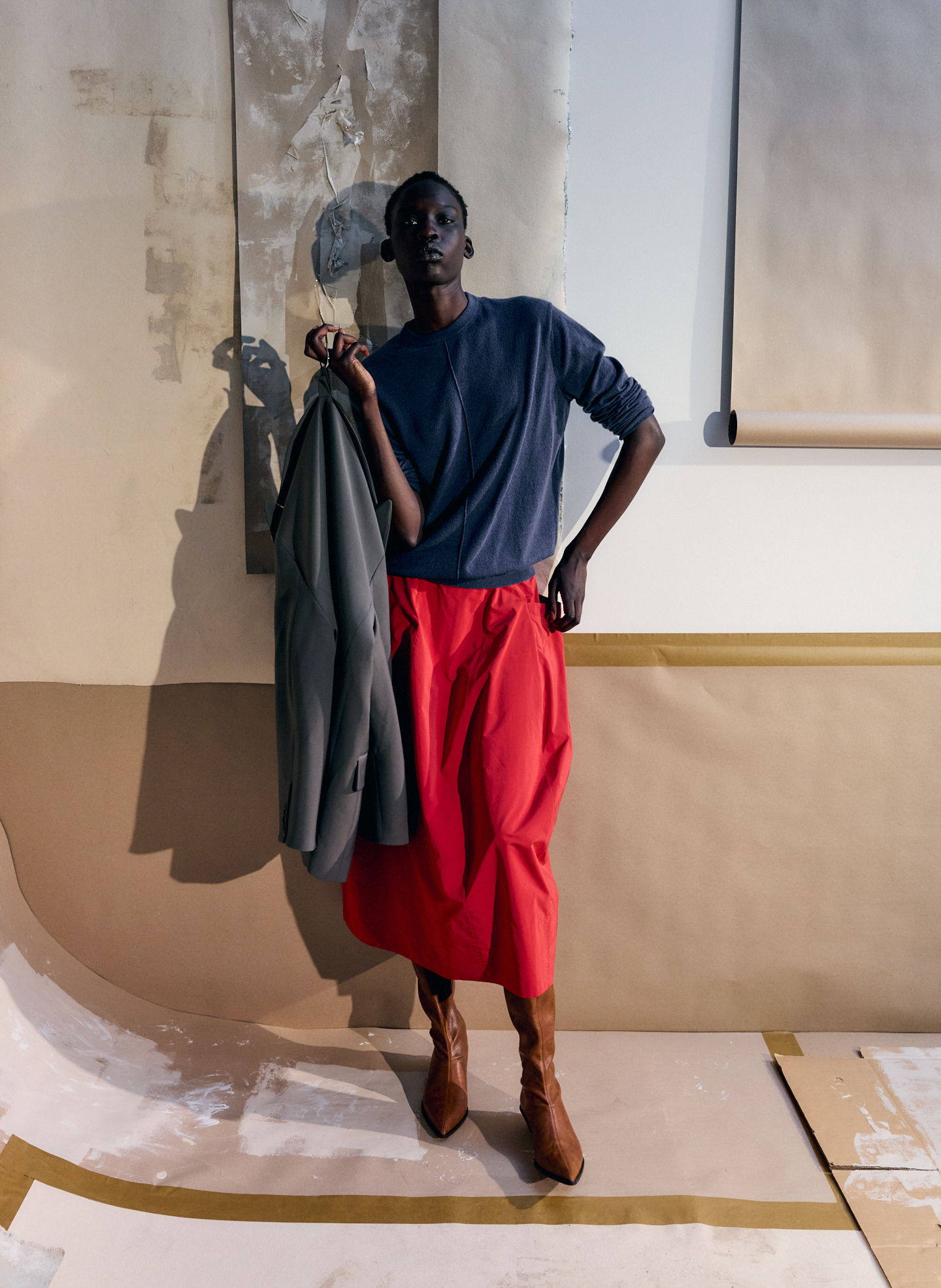 Model in a navy top and red skirt holding a jacket against a backdrop.