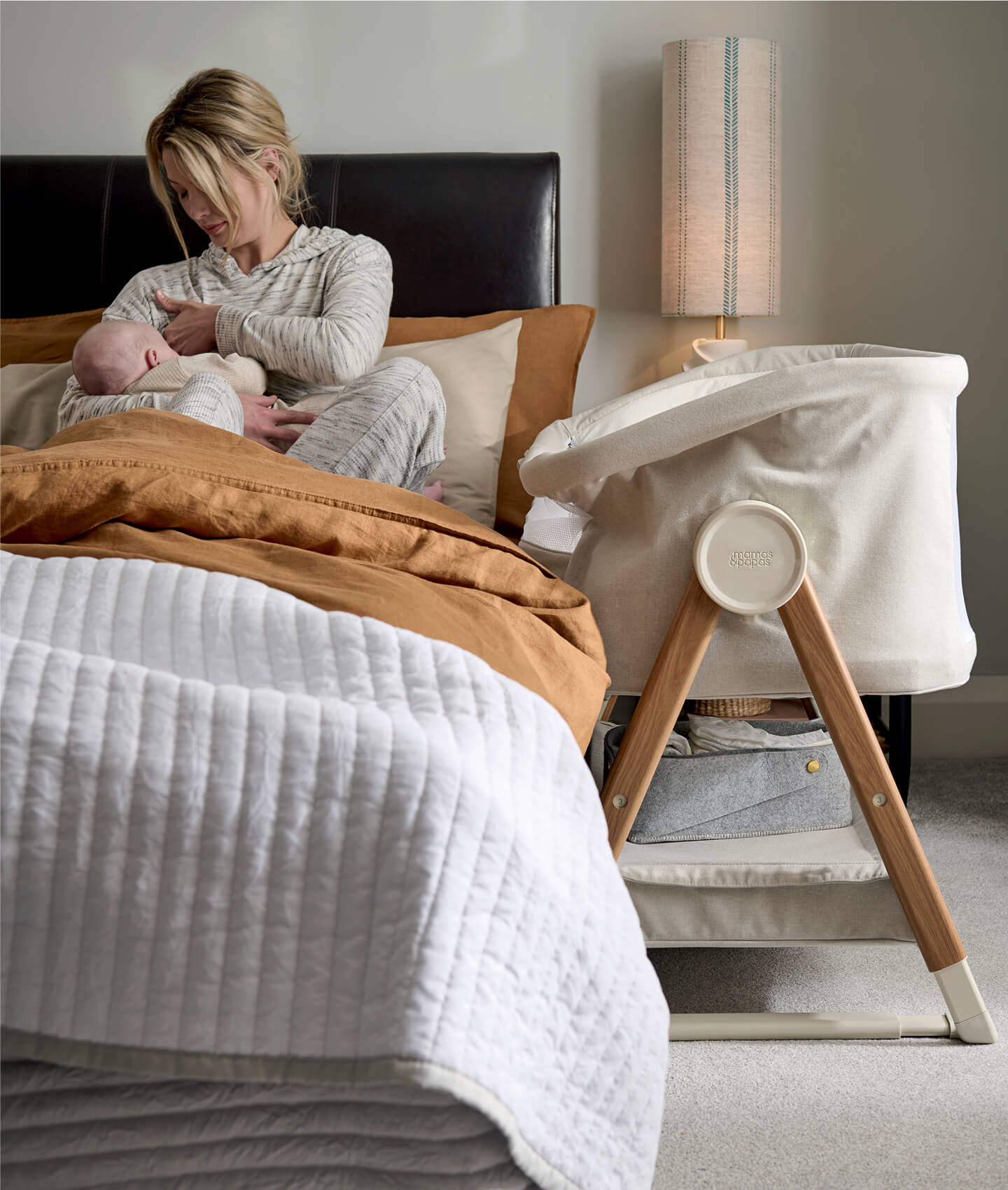 Woman sitting on a bed breastfeeding a baby next to a bassinet.