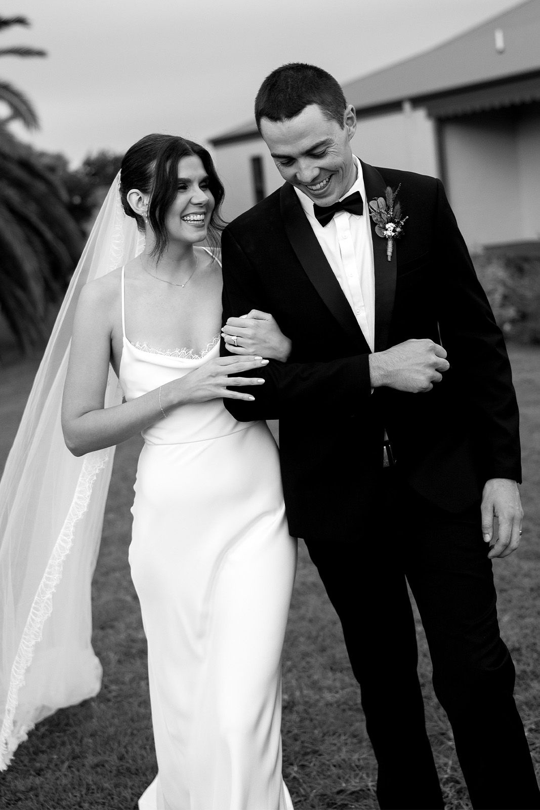 Bride and groom walking together, smiling, in elegant wedding attire.