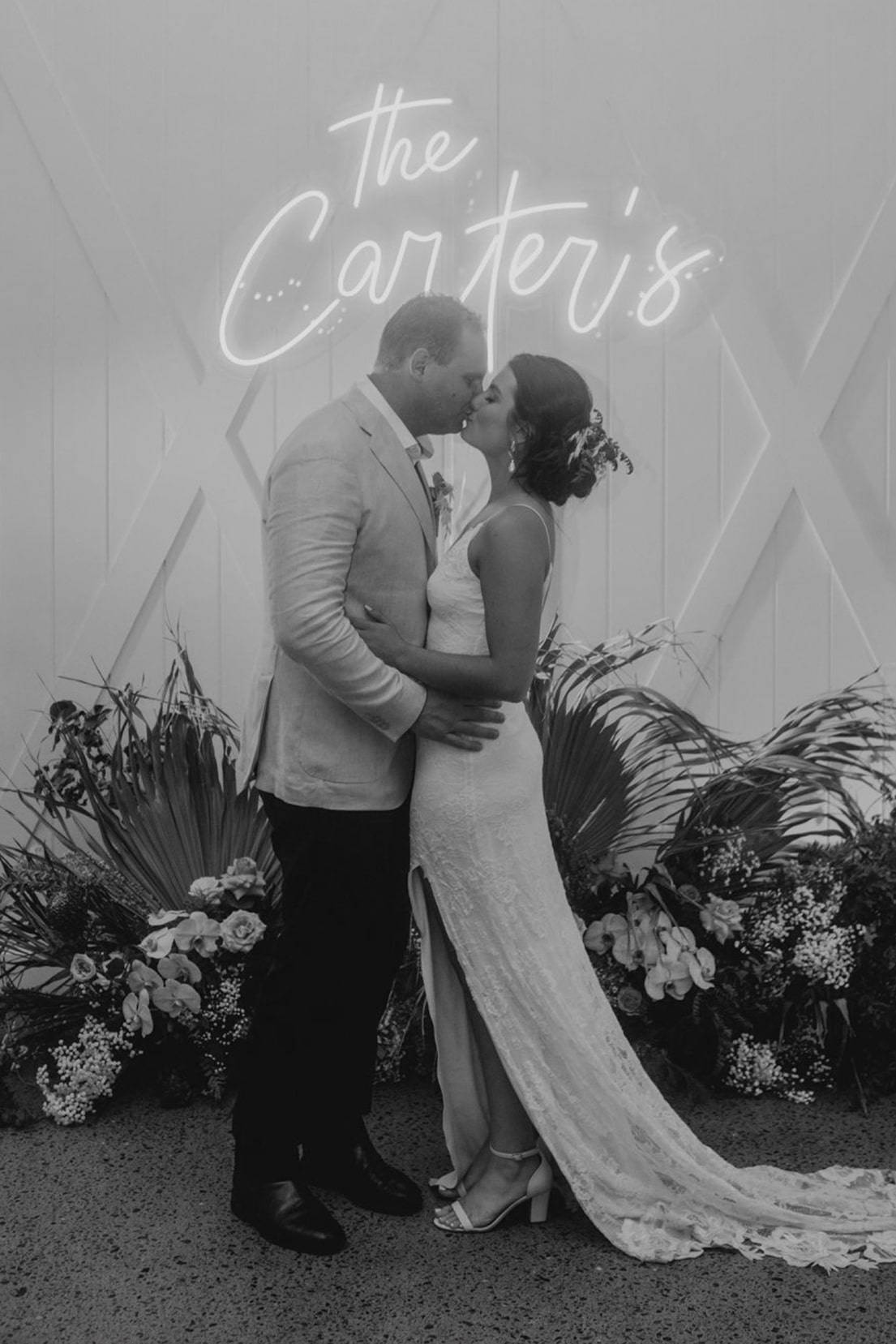 Bride and groom kissing underneath a neon sign