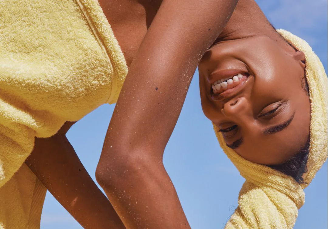 Smiling person in a yellow towel against a blue sky background.