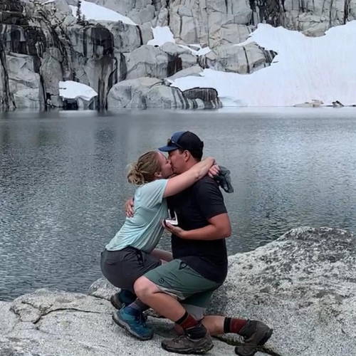 Featured couple at the sight of their proposal location kissing and hugging