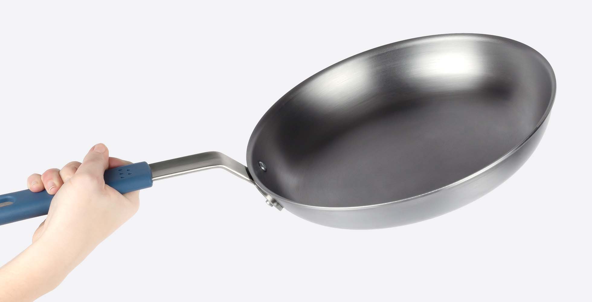 A close view of the Misen Carbon Steel Pan’s durable material, with a hand visible gripping the removable silicone handle grip.