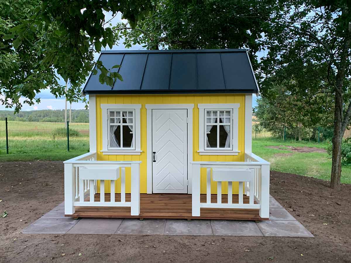 Yellow Kids Wooden Playhouse with black metal roof,  white fishbone door and flower boxes in the backyard by WholeWoodPlayhouses