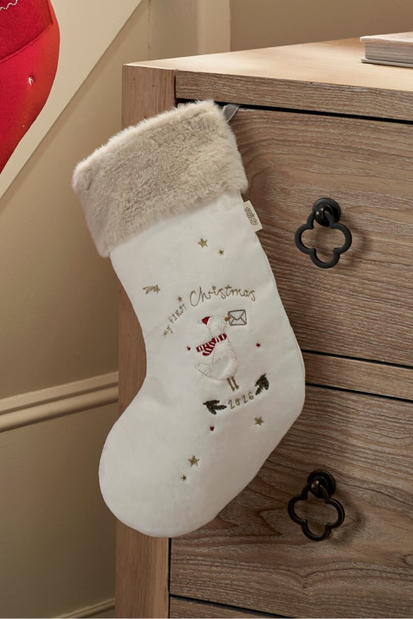 White Christmas stocking with decorative elements hanging from a wooden dresser.