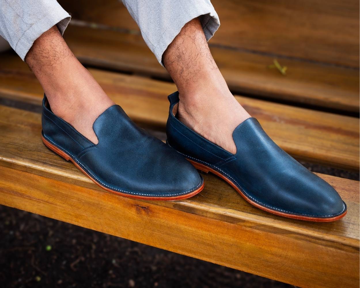 A man wearing Adelante navy blue leather wide width slip-on shoes while resting his feet on a wooden bench.