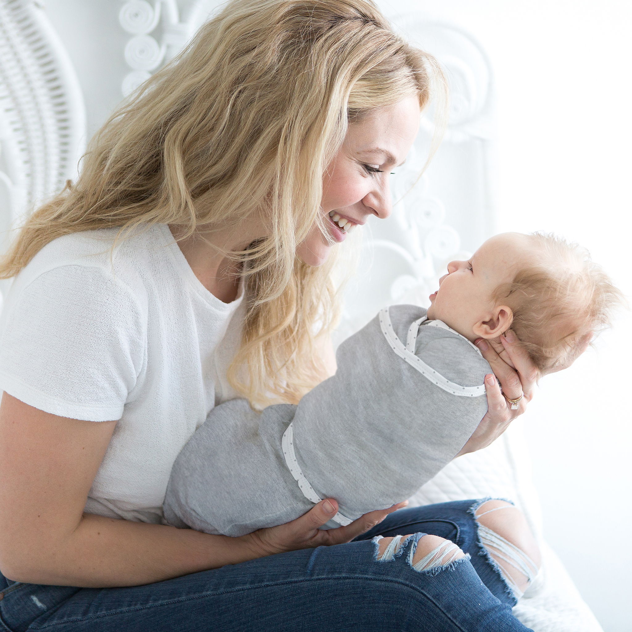 A mother smiles down at her baby wrapped in a heathered gray omni swaddle sack