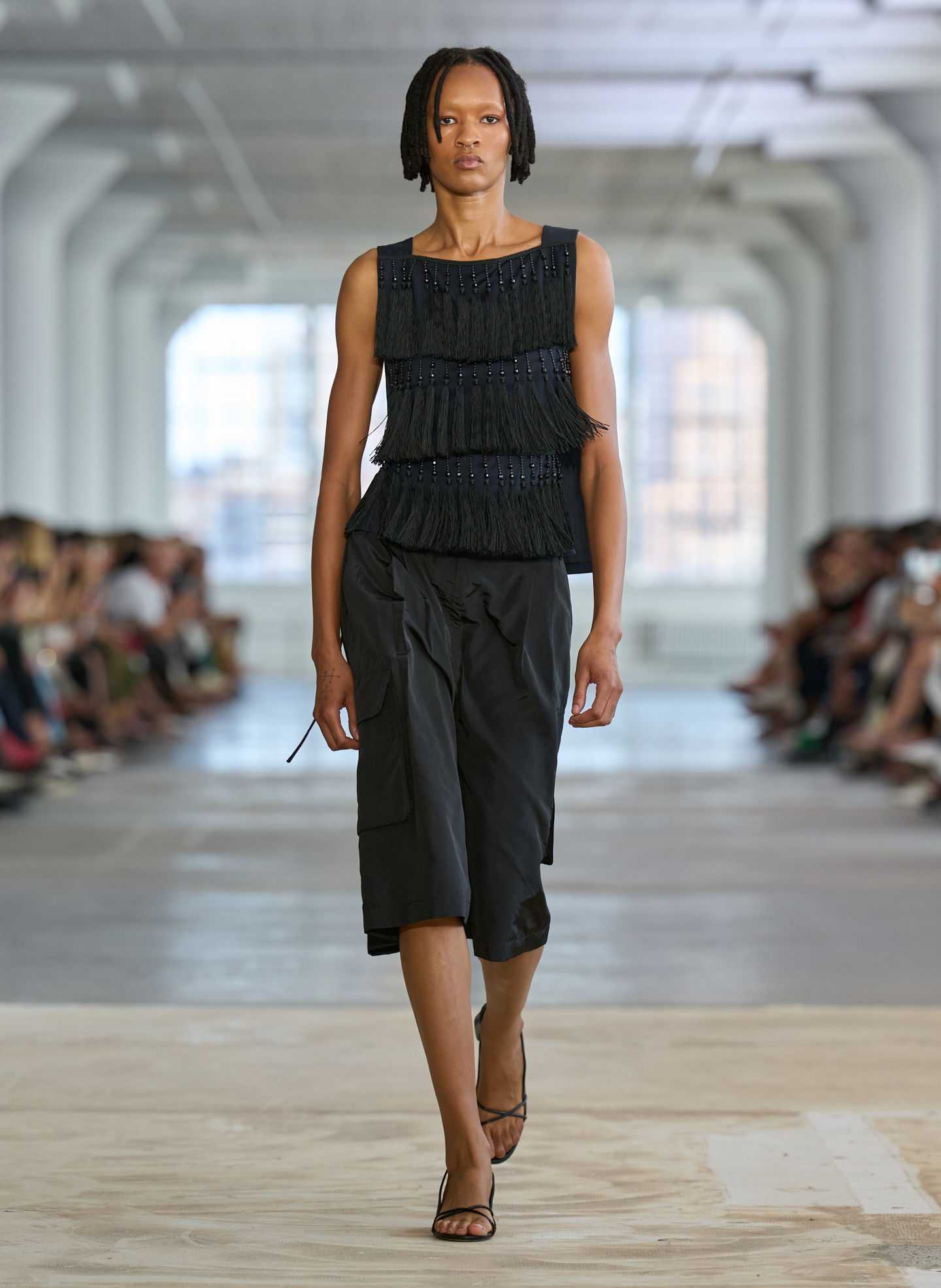 A model walks the runway in a fashion show wearing a black outfit.