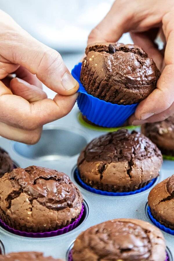 Chocolate muffins in a tray, with one being removed from the cake case.