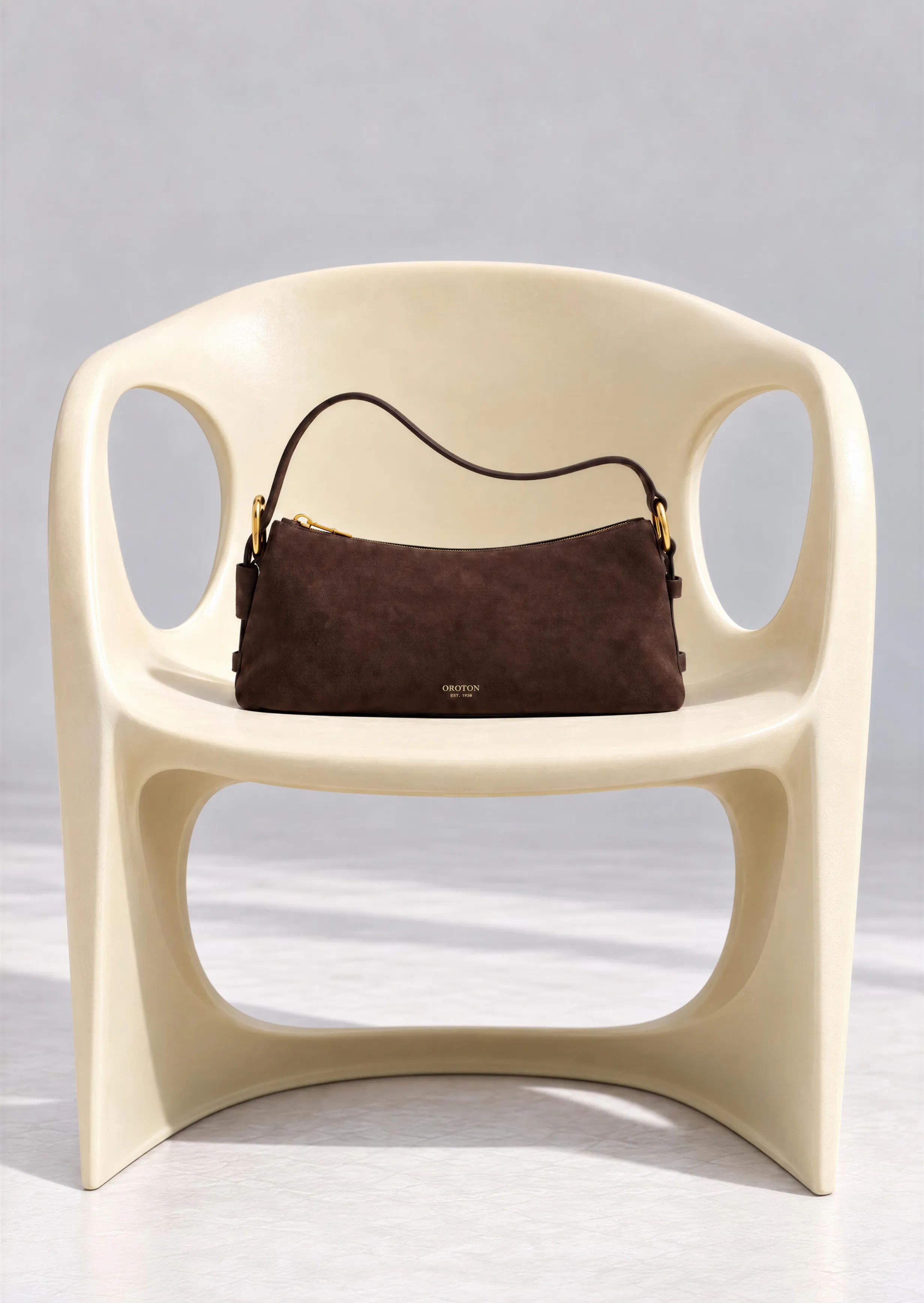 A brown suede handbag resting on a minimalist cream chair.