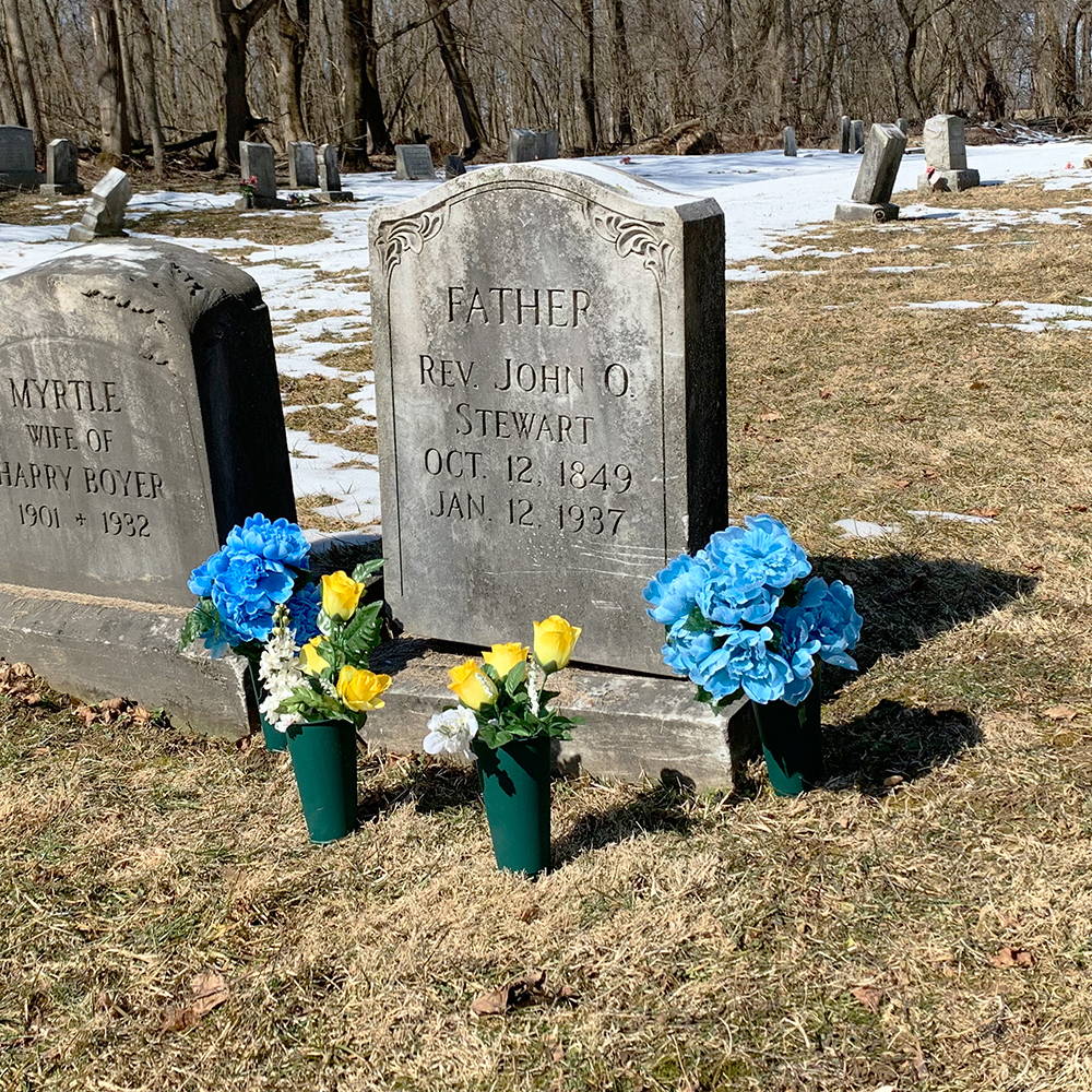 Flowers arranged in several memorial cemetery vases next to a gravestone