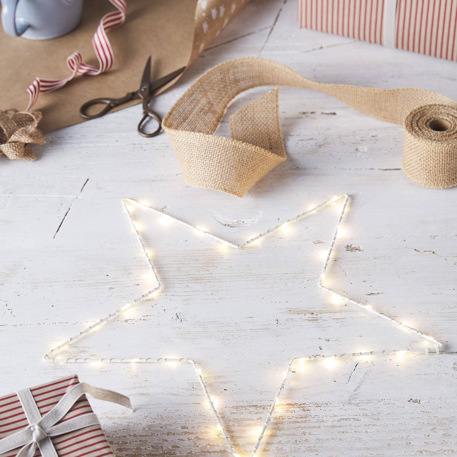 A light up Osby star on a white wooden table with gift wrapping material.