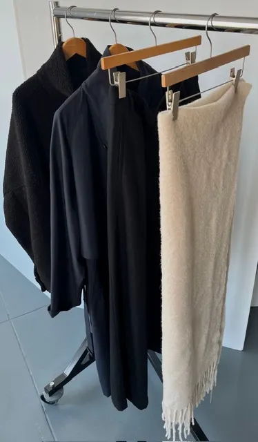 Three garments hanging on a rack: two dark outfits and a light blanket.