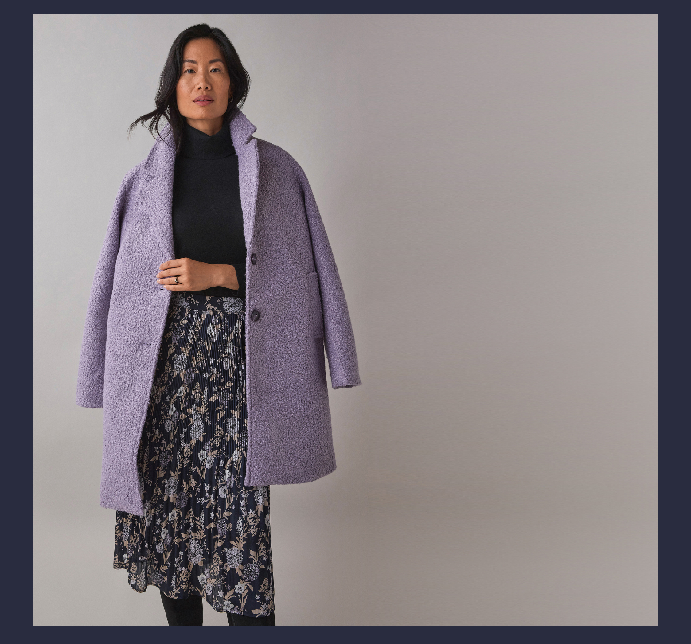 Woman wearing a purple coat and floral skirt against a neutral background.