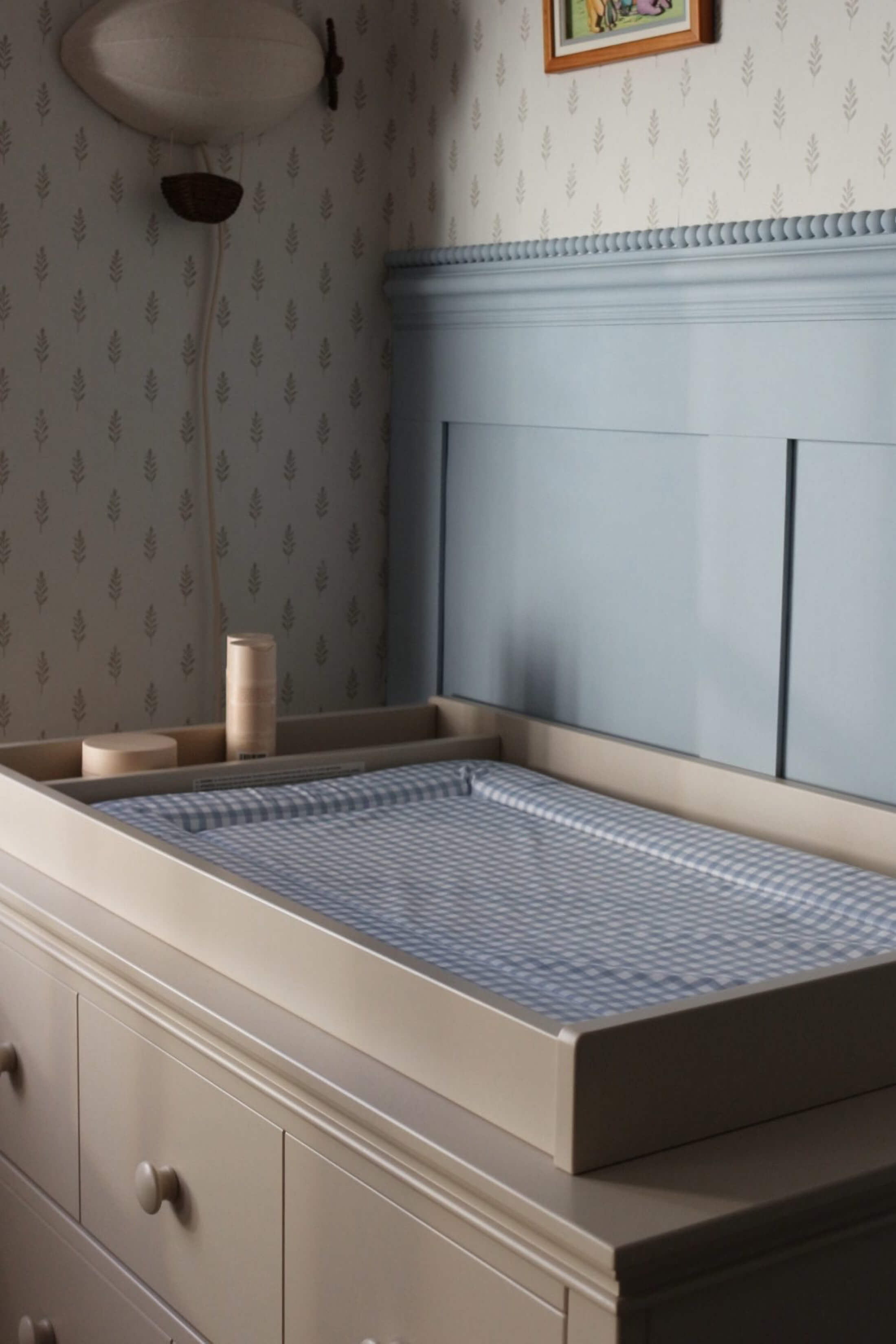 Changing table in a softly lit nursery with patterned wallpaper.