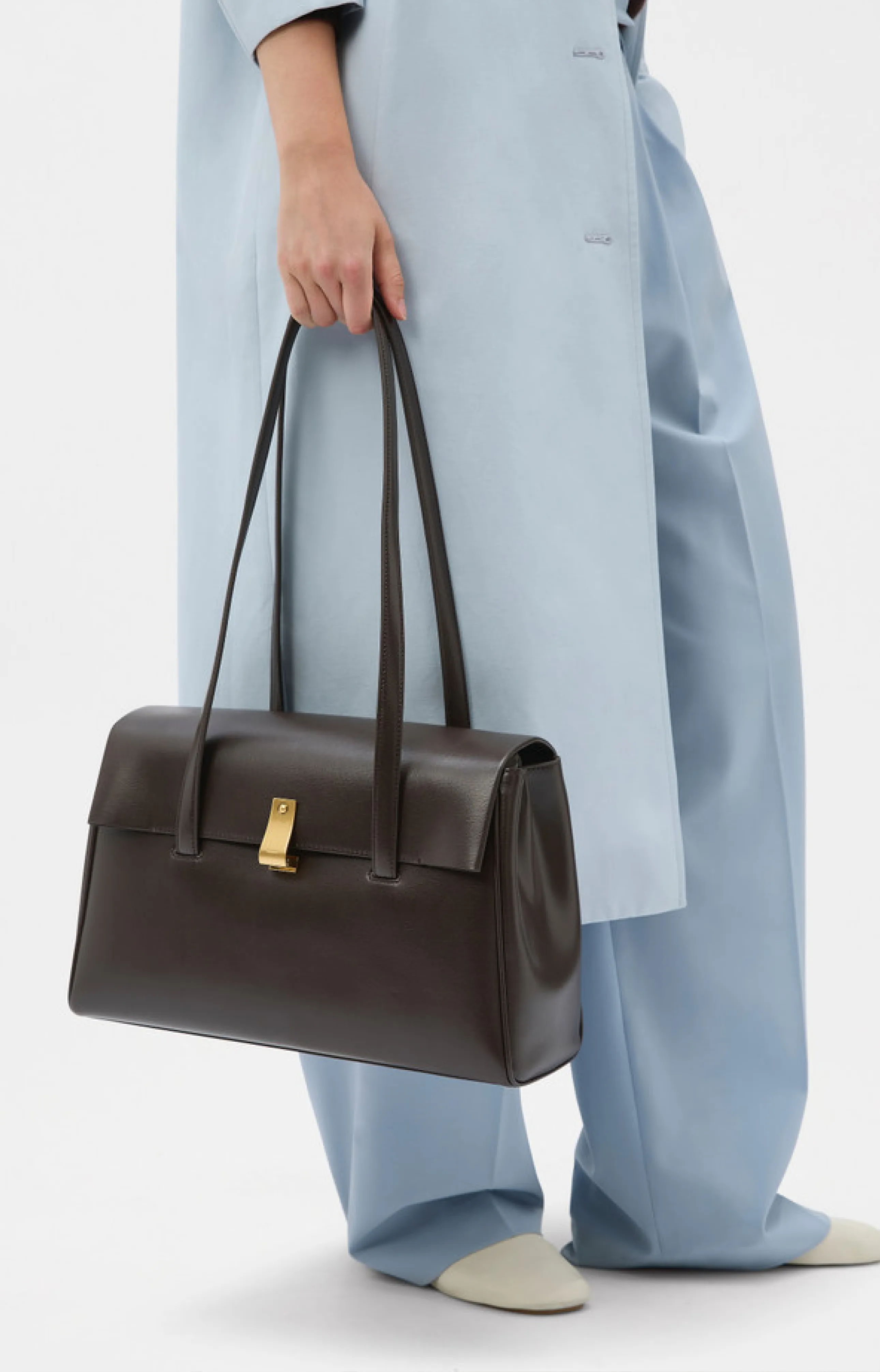 Person holding a dark brown handbag, wearing light blue outfit and shoes.