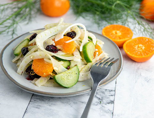 A plate of salad with cucumber, oranges, and dried fruits.