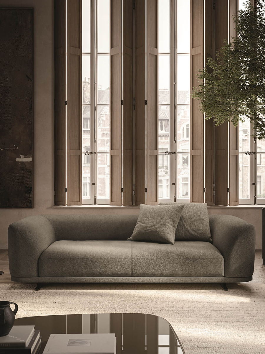 A modern Aurel sofa with cushions in a well-lit room with large windows.