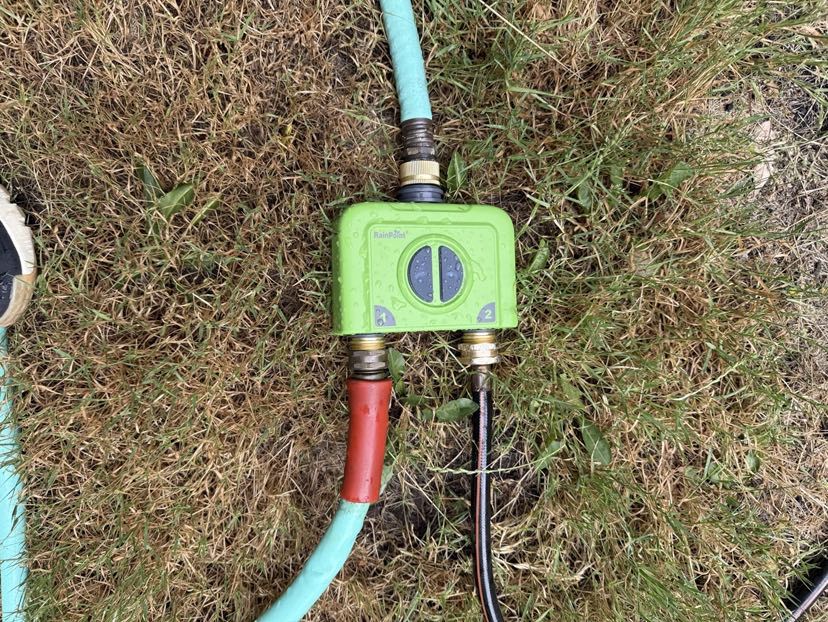 Green valve connected to hoses on grass.