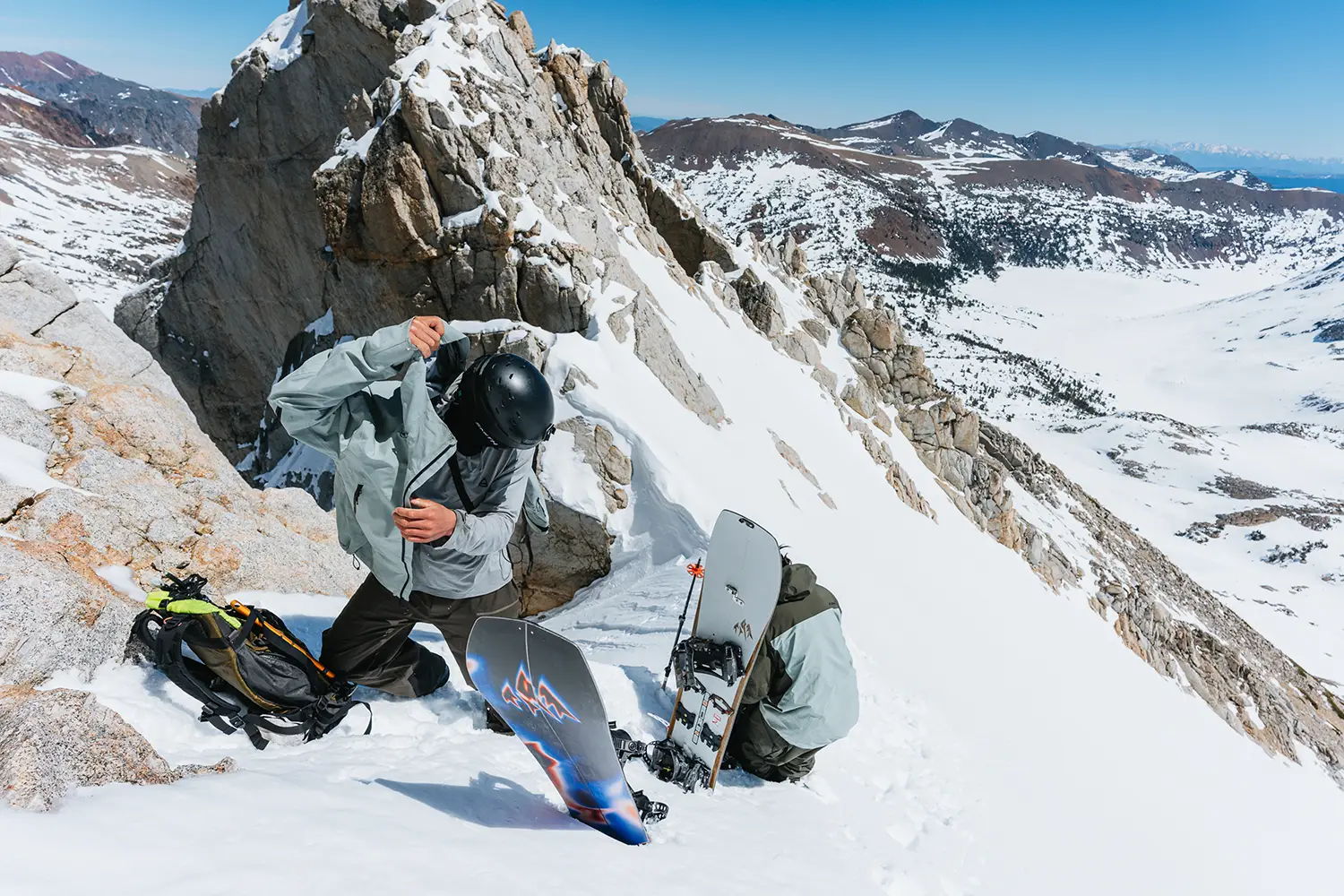 Snowboarder adjusting gear on a snowy mountain peak with scenic views.