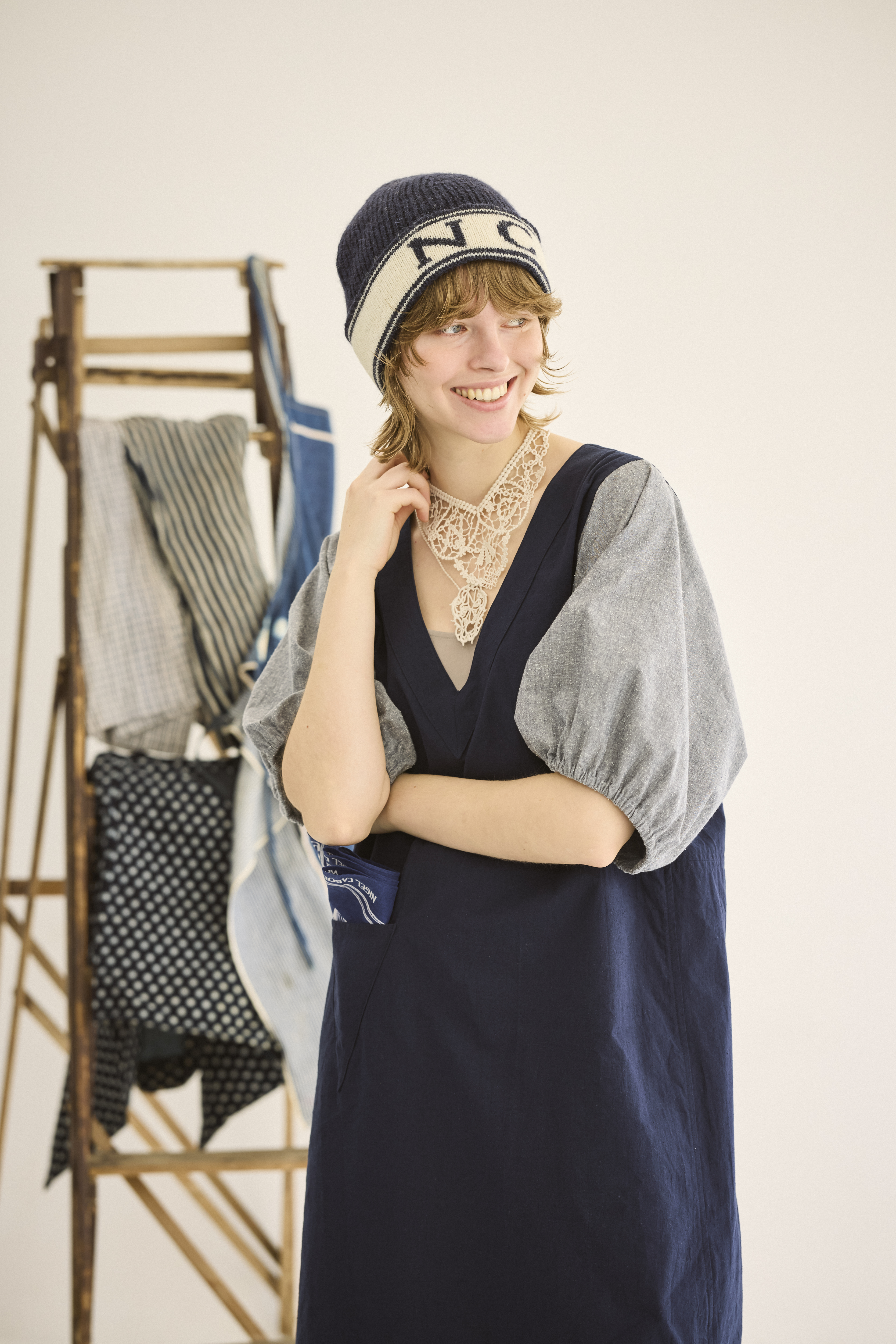A person in a stylish outfit with a hat and jewelry posing indoors.