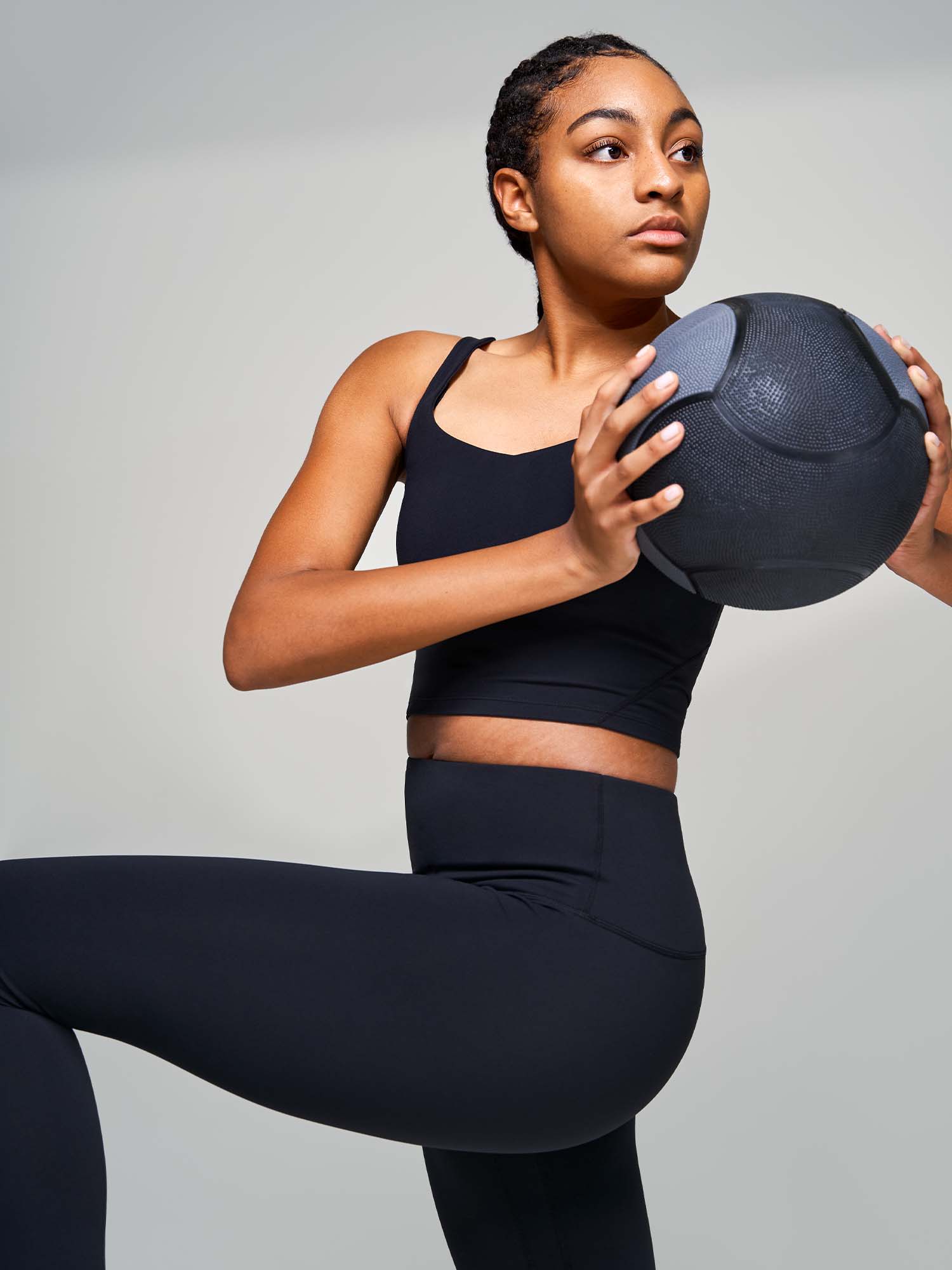Tall woman wearing a black tank top and leggings holding a medicine ball and twisting
