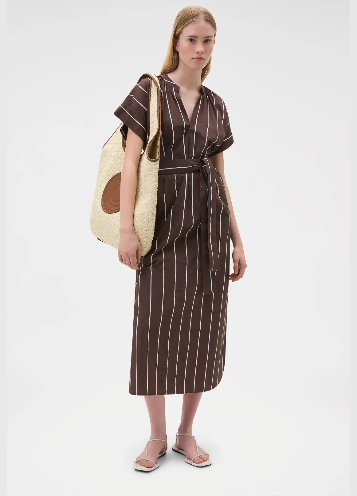 Woman in a brown striped dress with a large tote bag.