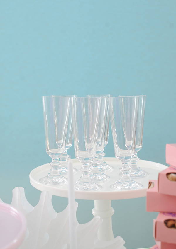 Glass champagne flutes on a cake stand against a blue background.