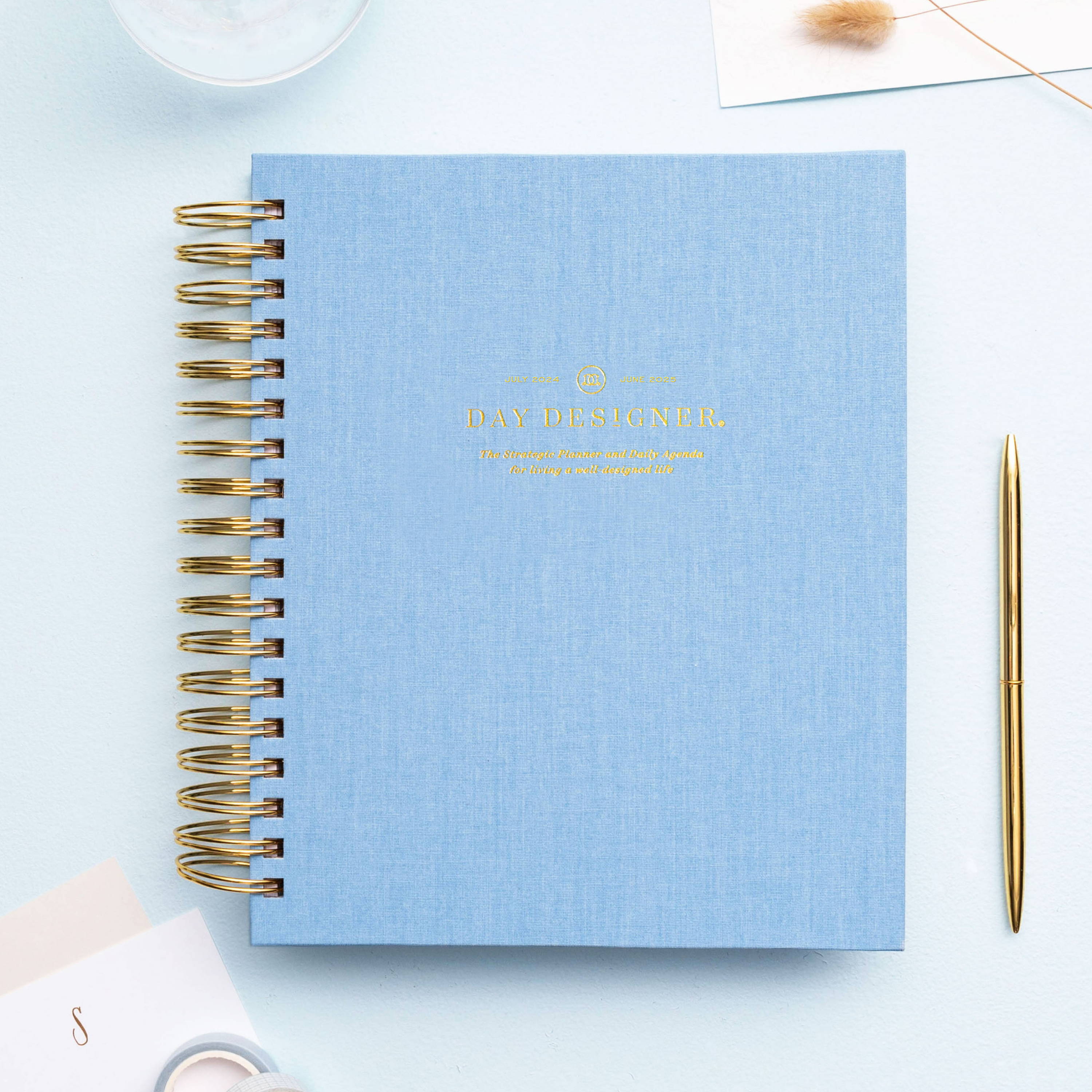 light blue closed book bookcloth planner on light blue background, gold pen, stationery, dried flower