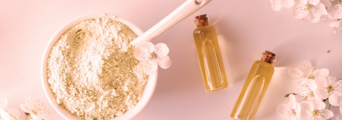 Bowl of powder and small bottles on a pink background with flowers.