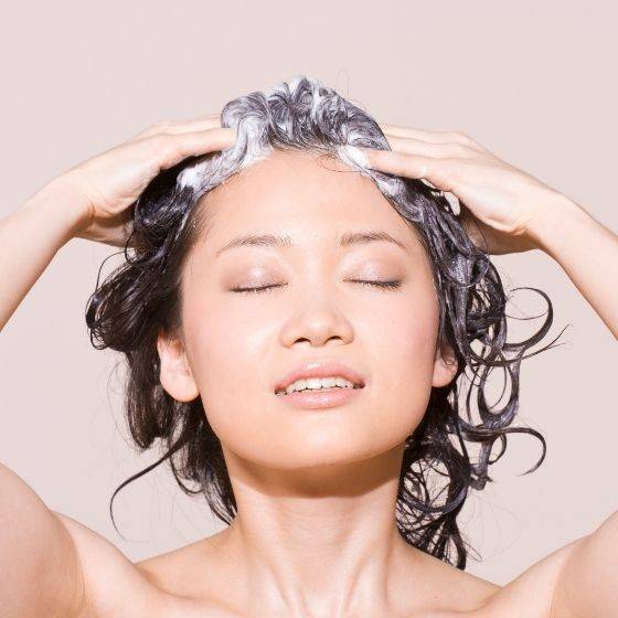 Woman with eyes closed enjoying foaming hair with hands
