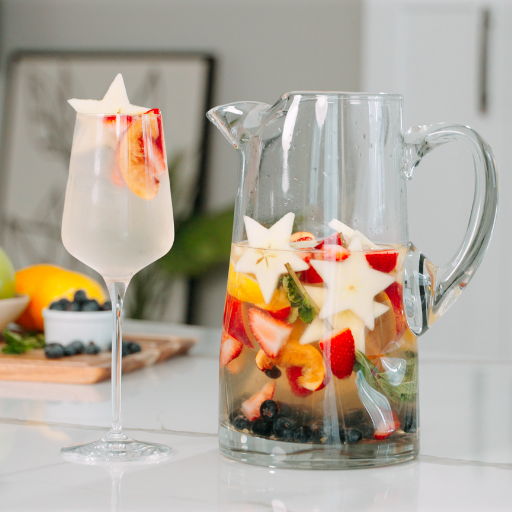A glass of fruit-infused drink next to a pitcher with fruit.