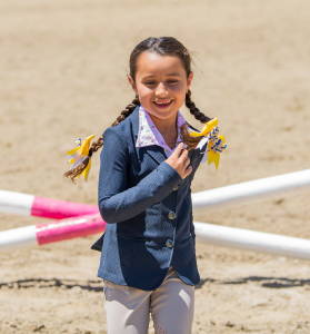 Young Equestrian wearing a show outfit with show bows running towards the camera. Shop all kids at TriedEq.