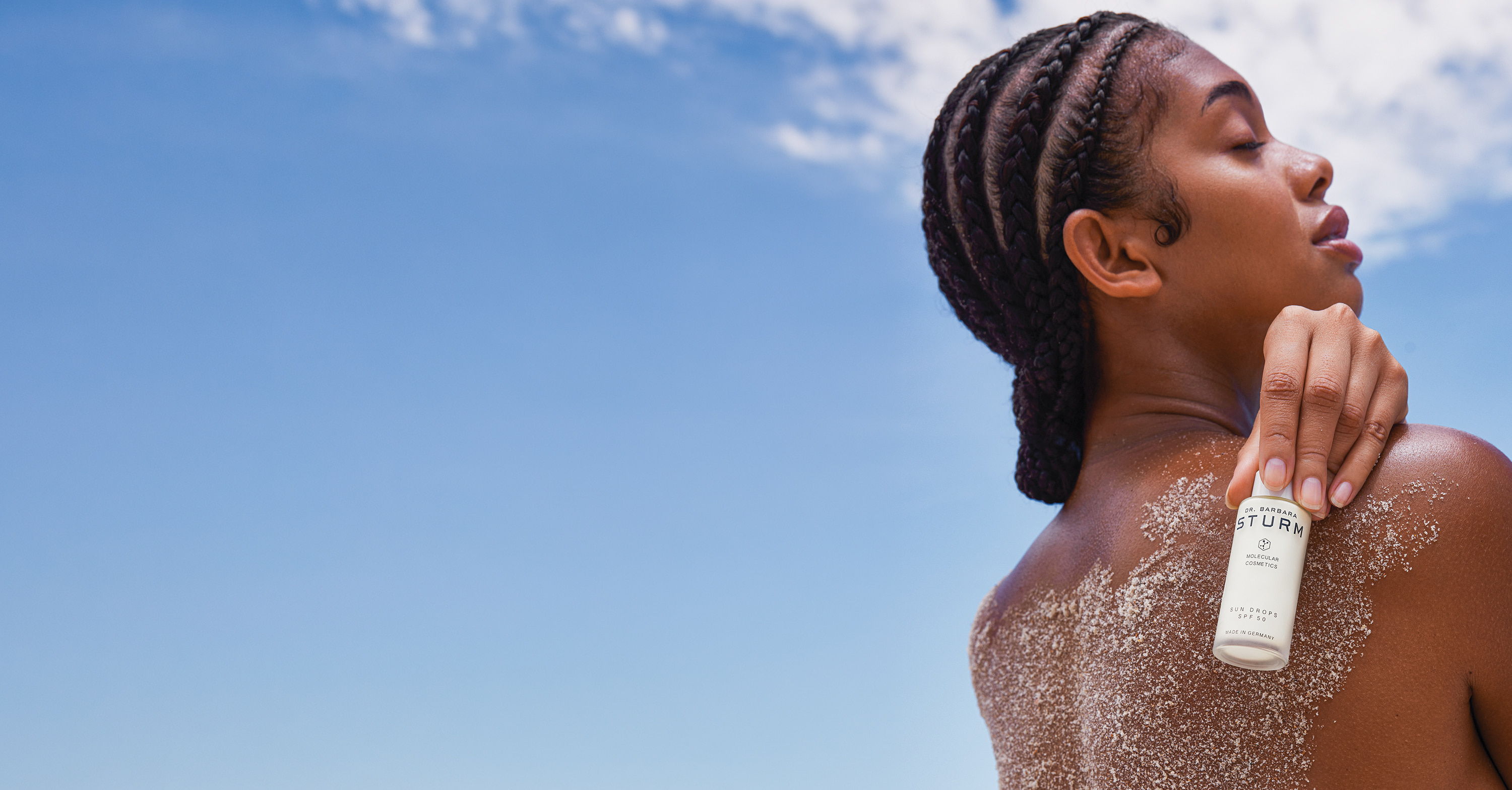 Person applying lotion on their back against a clear blue sky.