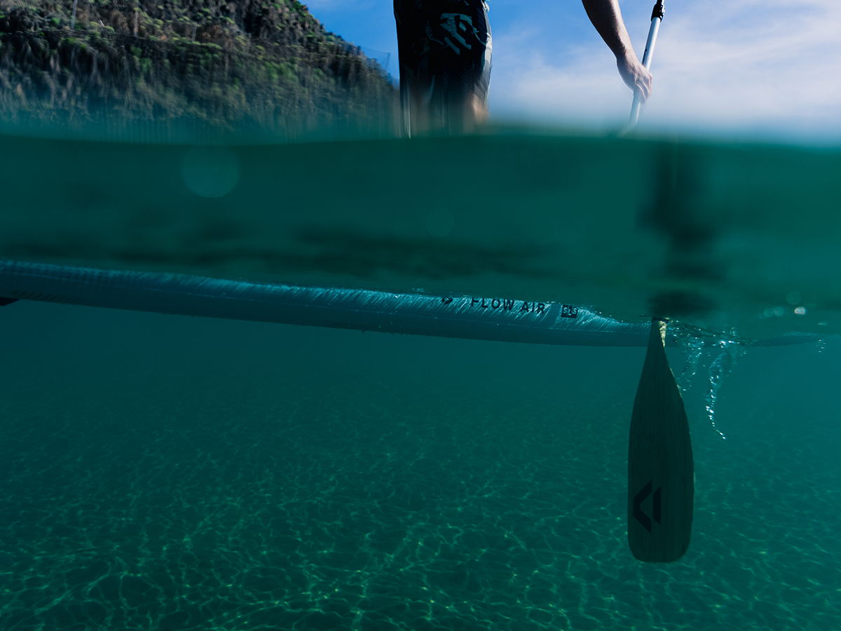 Person paddleboarding with a submerged paddle in clear water.