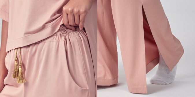 Woman holding a pink garment with a pocket, wearing light-colored pants.