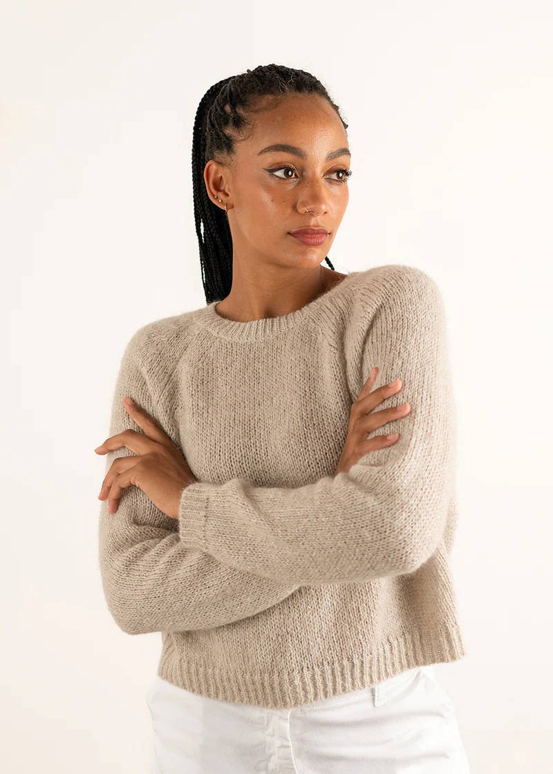 A model wearing an off white, wool blend long sleeved jumper over white trousers