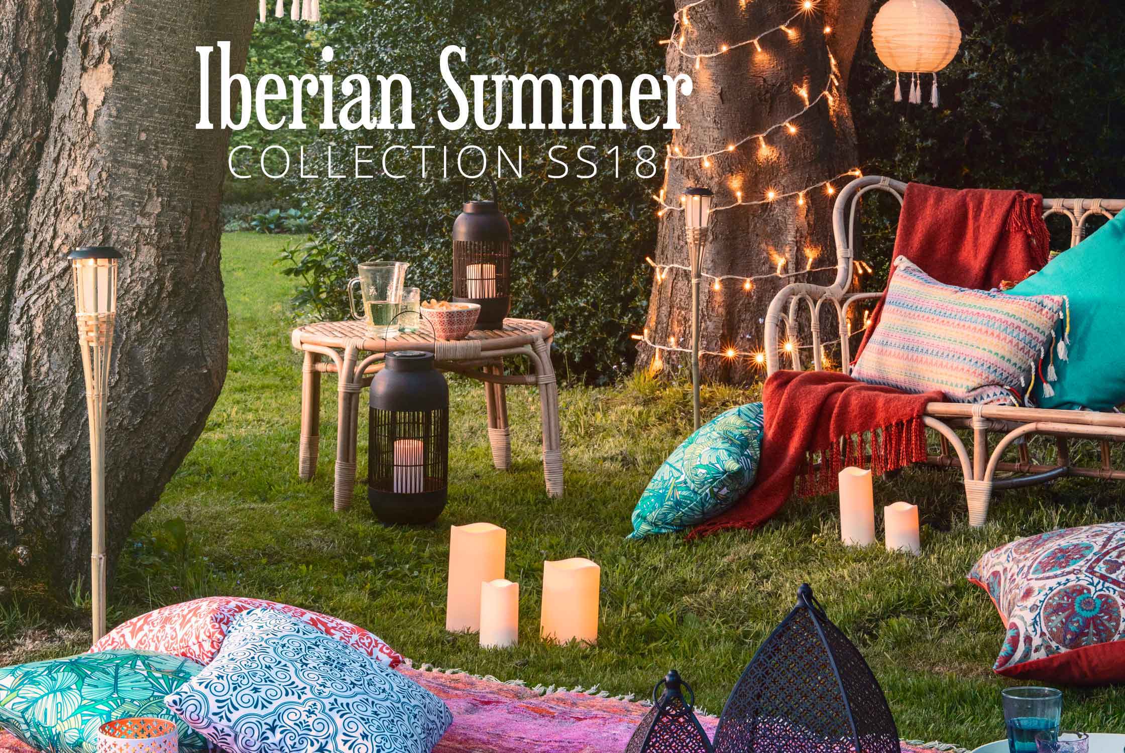 An outdoor summer setting of lanterns and candles with cushions and throws.