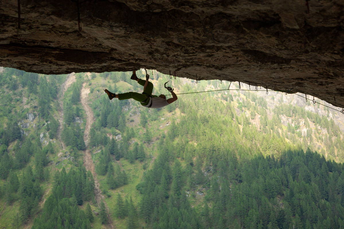 Silhouette of rock climber climbing horizontally below the rocks, with tree below