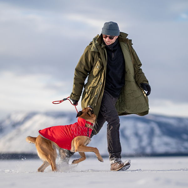 Person walking a dog in a red coat on snowy landscape.