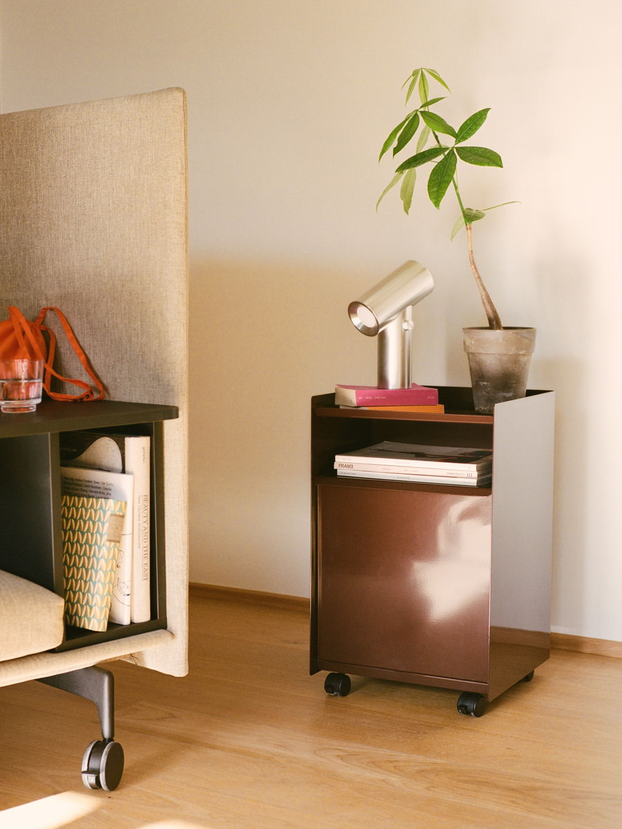 A brown Folded Muuto rolling cart with a lamp and a potted plant.