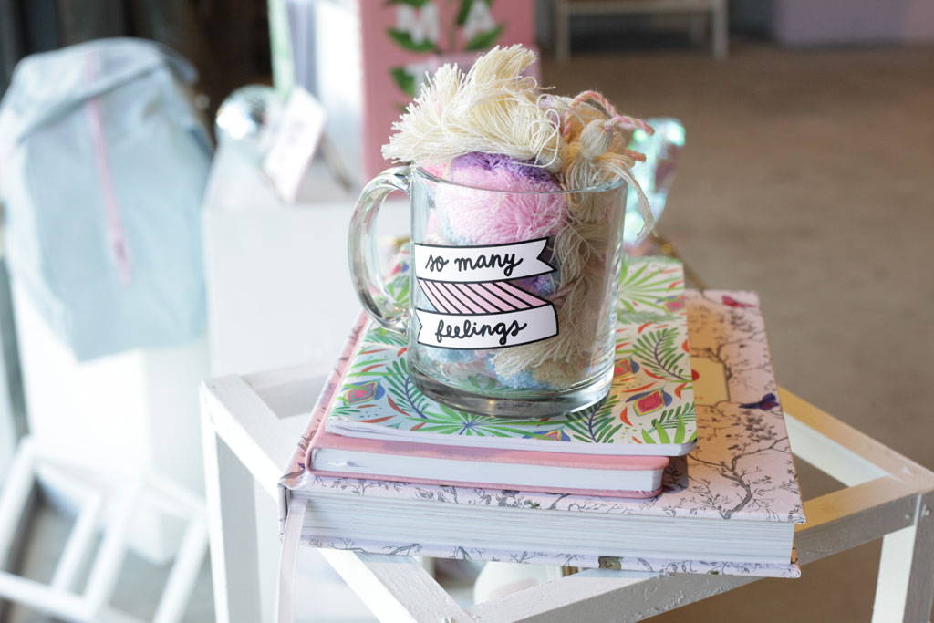 A funny coffee mug with pom poms sitting on a pile of books.