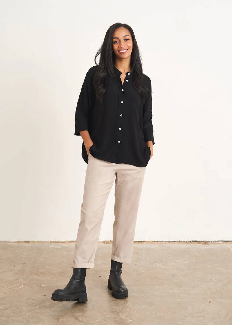 A model wearing a black button up oversized shirt with off white trousers and black leather chelsea boots 