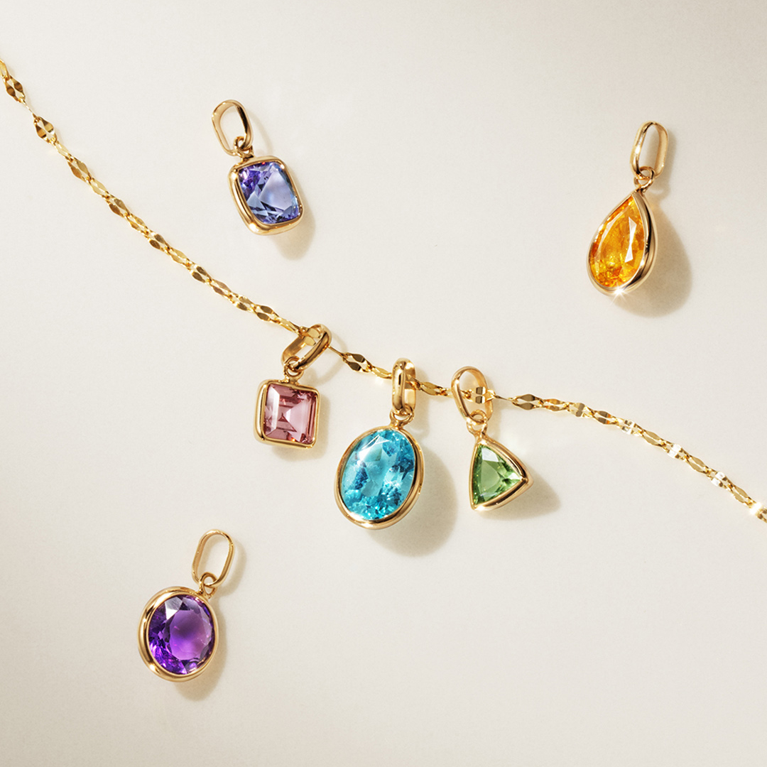 Gold chain with colorful gemstone pendants displayed on a neutral background.