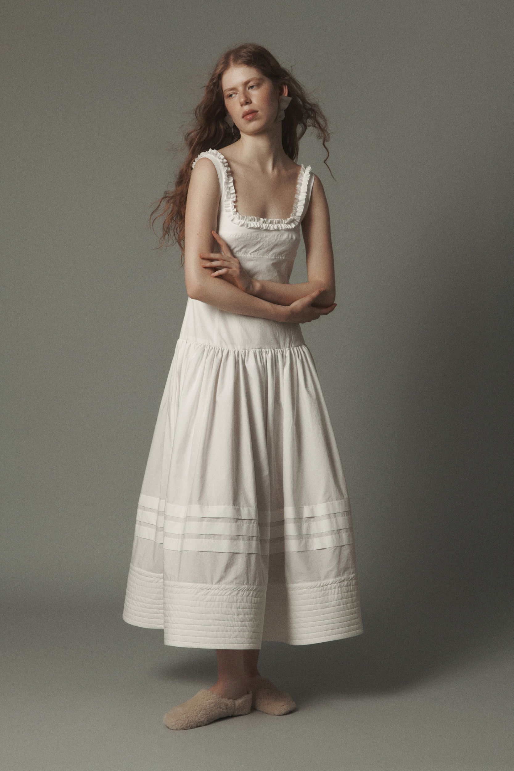A woman in a white dress poses against a gray background.