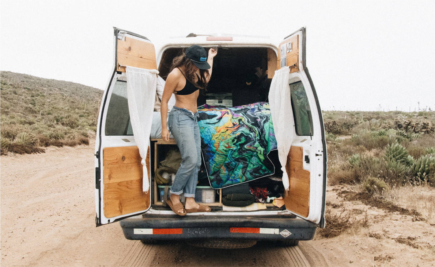 A woman stands in the back of a van with her Rumpl blanket, ready for a journey.